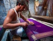 A woman draped in a vibrant silk saree stands against a backdrop of saree weaving looms, showcasing the intricate craftsmanship of traditional Indian sarees.